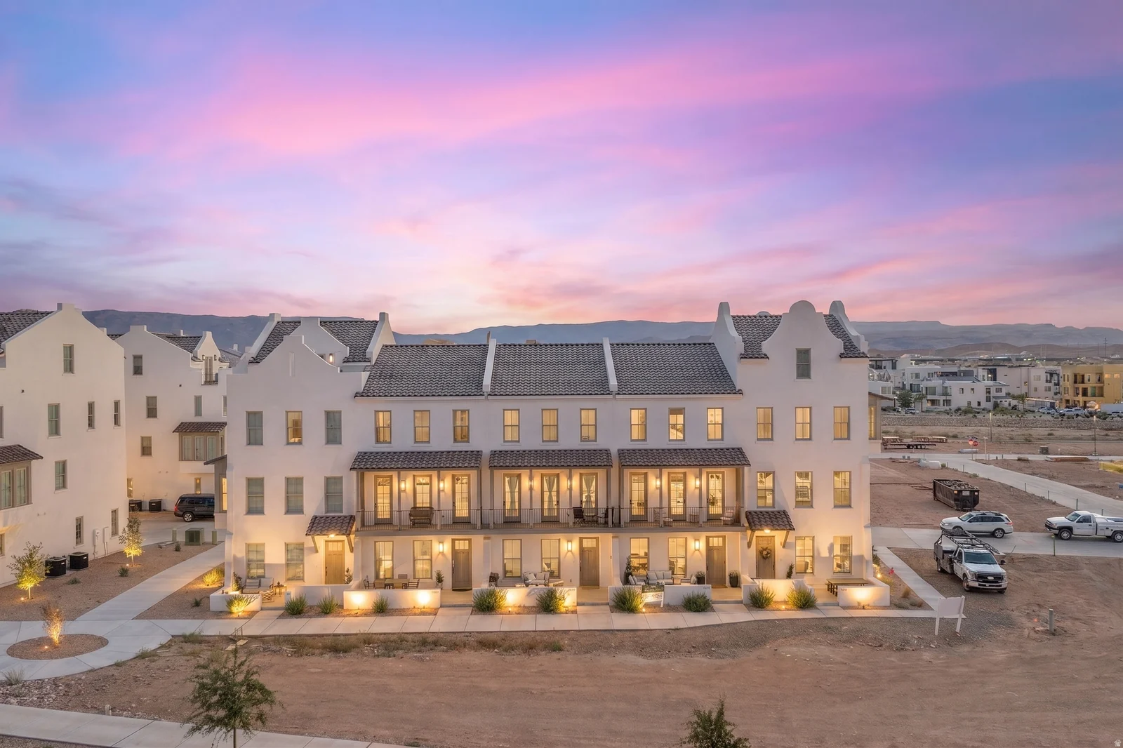 White stucco exterior with multiple levels, dark tile roofing, covered balconies, and exterior lighting fixtures
